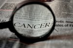 Newspaper headline under magnifying glass 'CANCER'