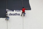 two hanging wall painters covering 'covid vax deaths'